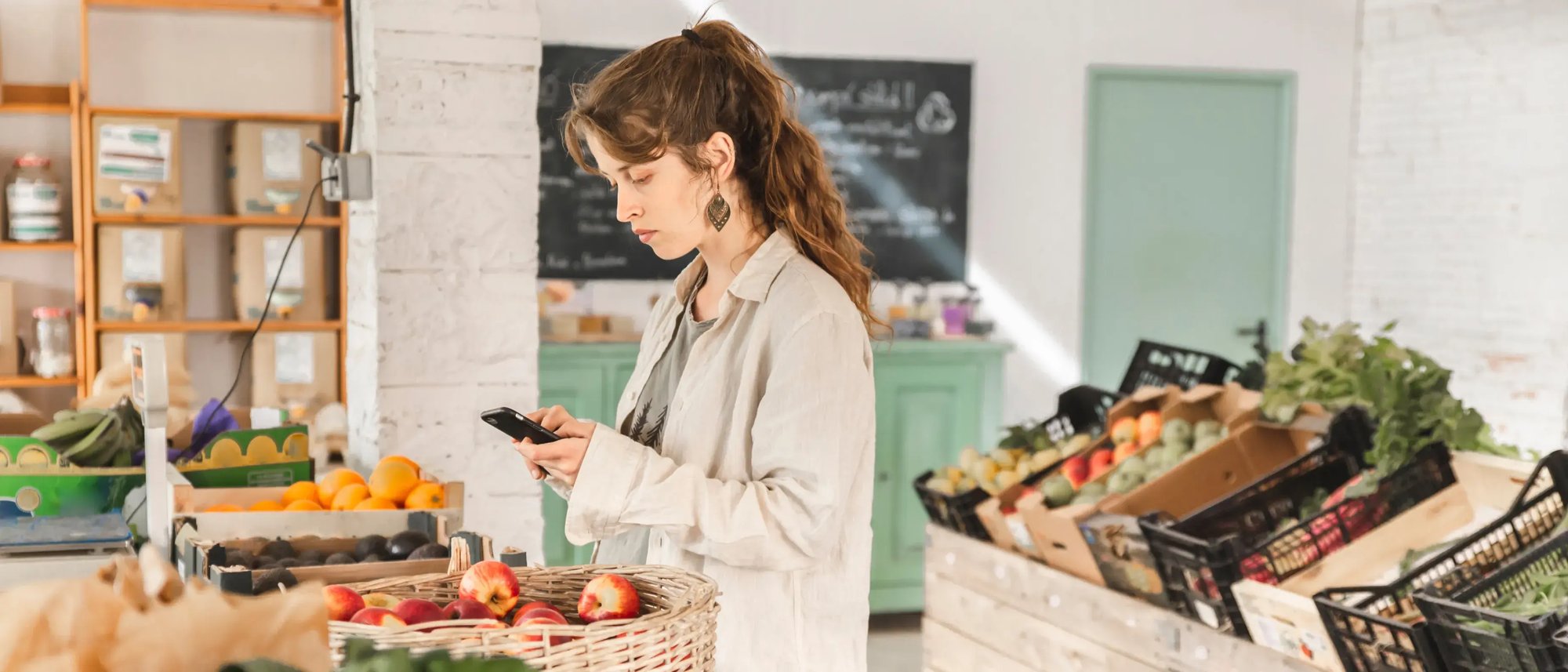 Woman using smartphone while grocery shopping in a fresh produce store.