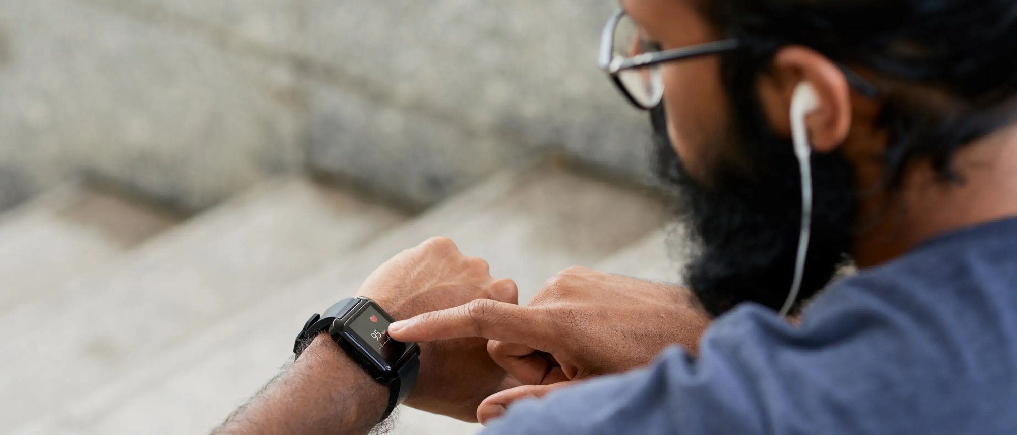 A man looks down at and taps his wearable device.
